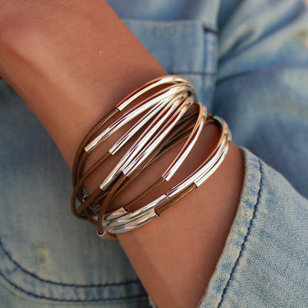 Close-up of a wrist wearing multiple metallic bracelets with a blurred denim background