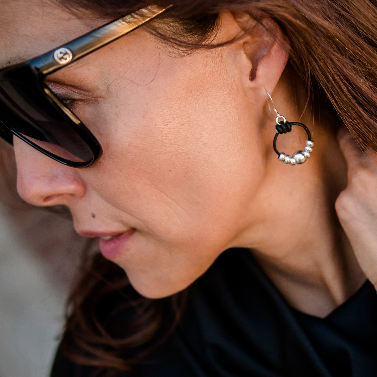 Close-up of a person wearing sunglasses and a black earring with beads.