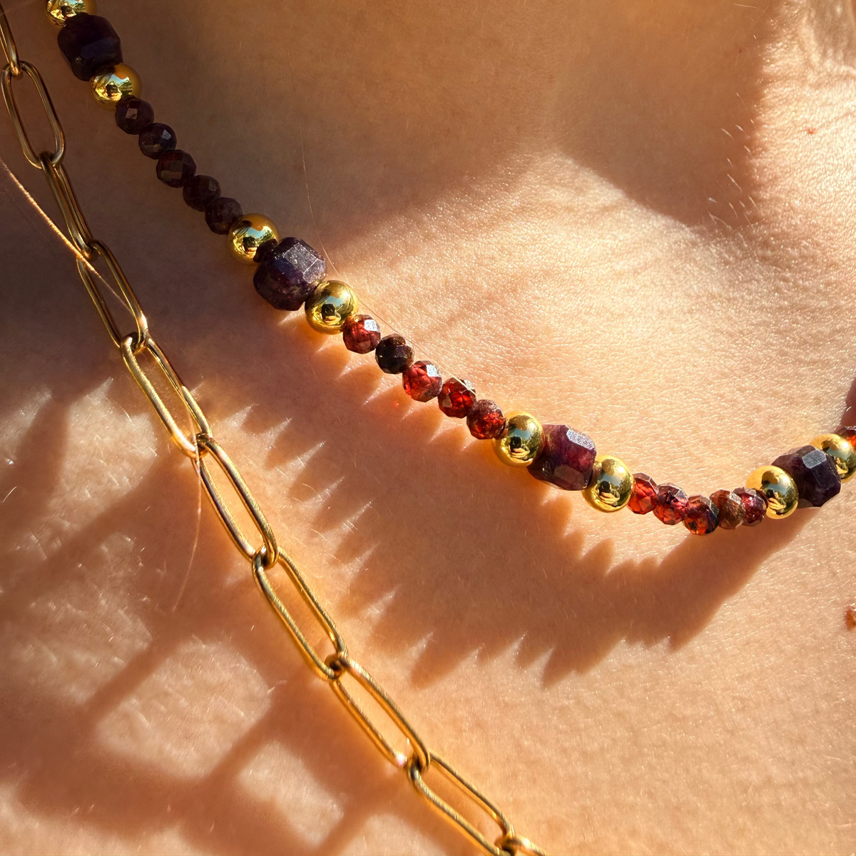 Close-up of a multicolored beaded necklace and gold chain on skin.