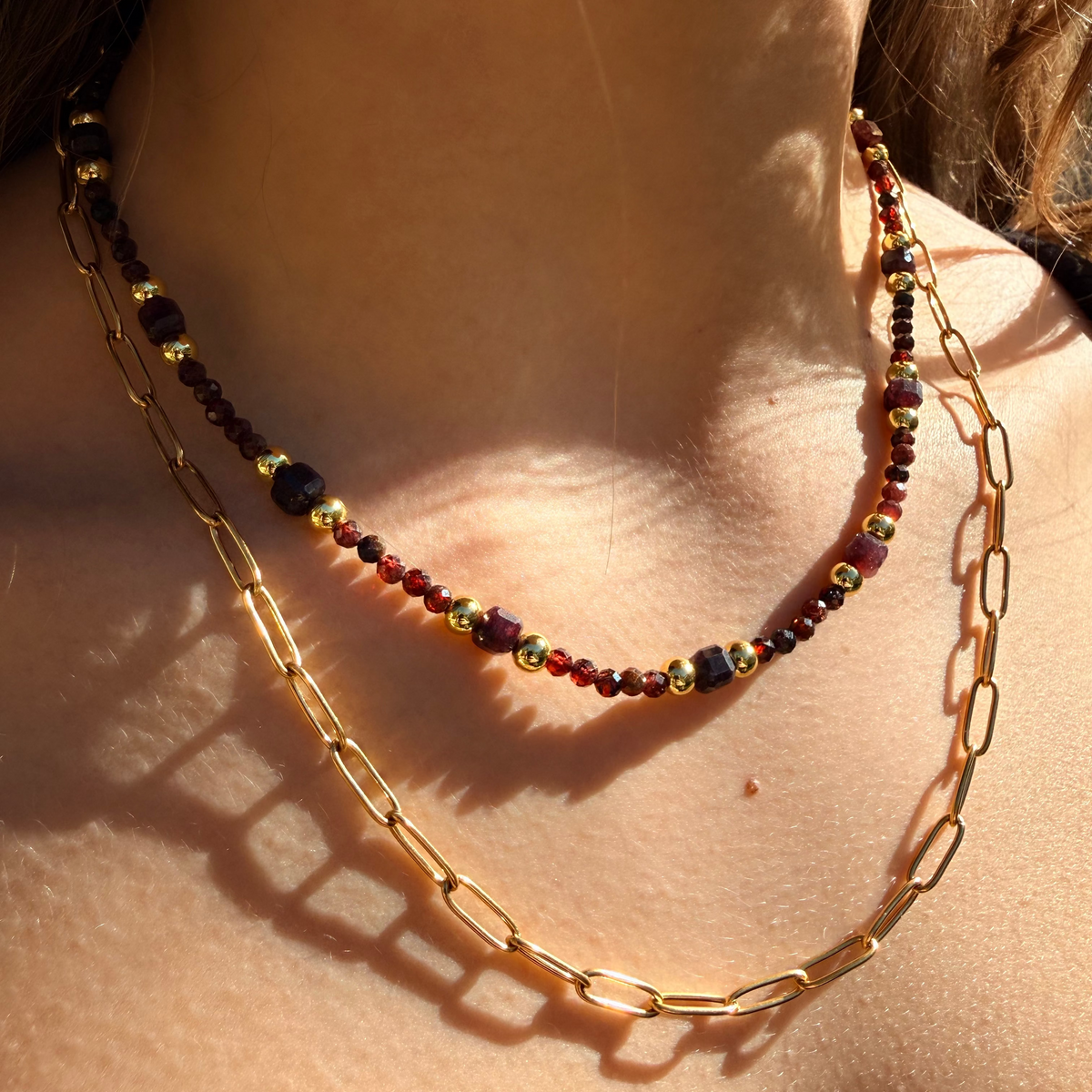 Two necklaces on a person's neck with sunlight casting shadows.