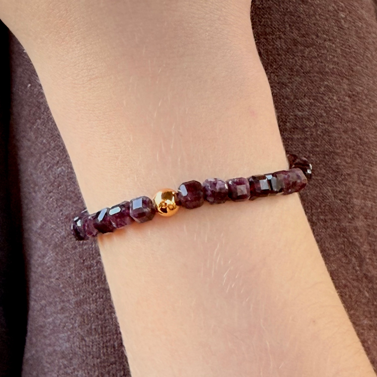 Bracelet with red beads on a wrist against a brown background