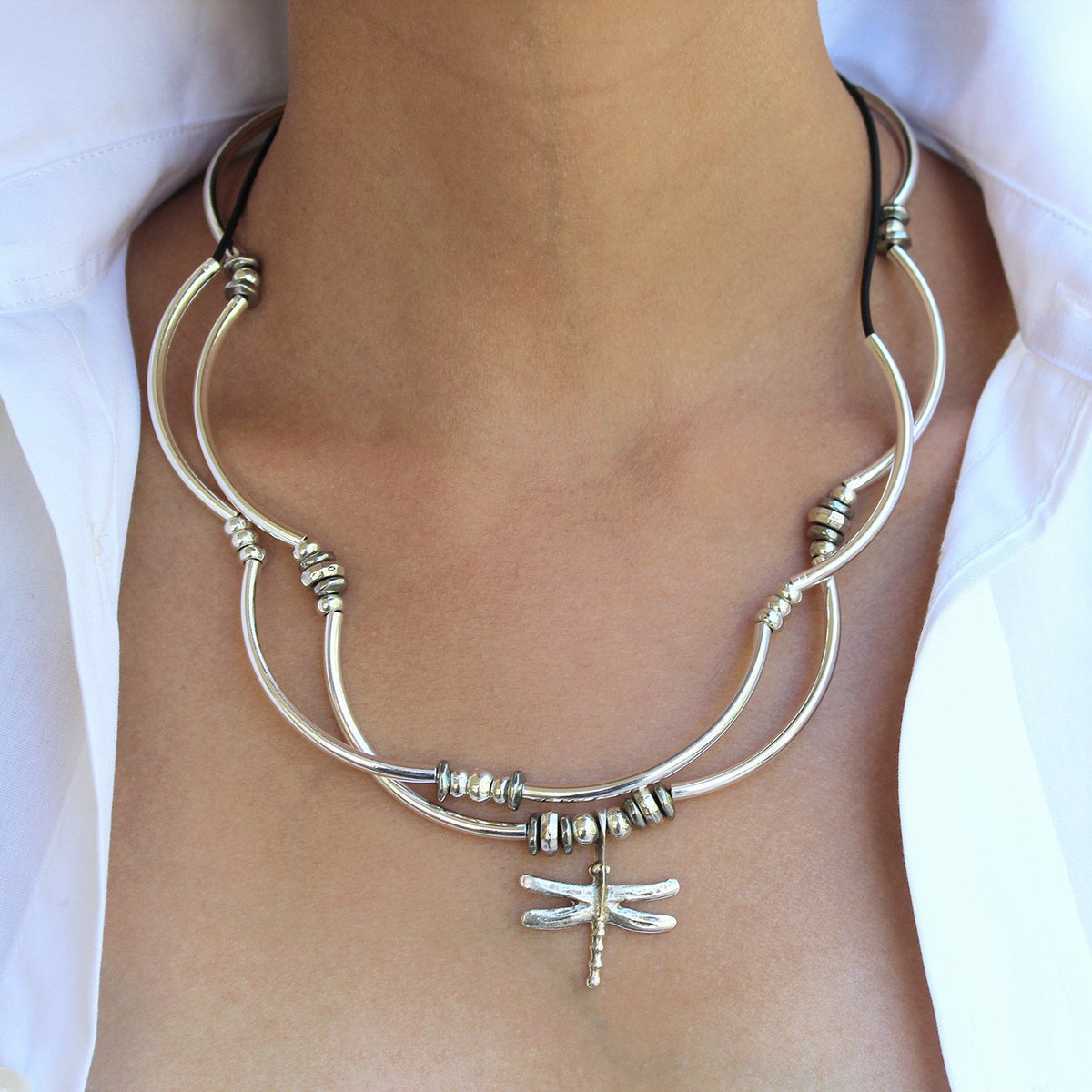 Silver necklace with dragonfly pendant on a person wearing a white shirt.