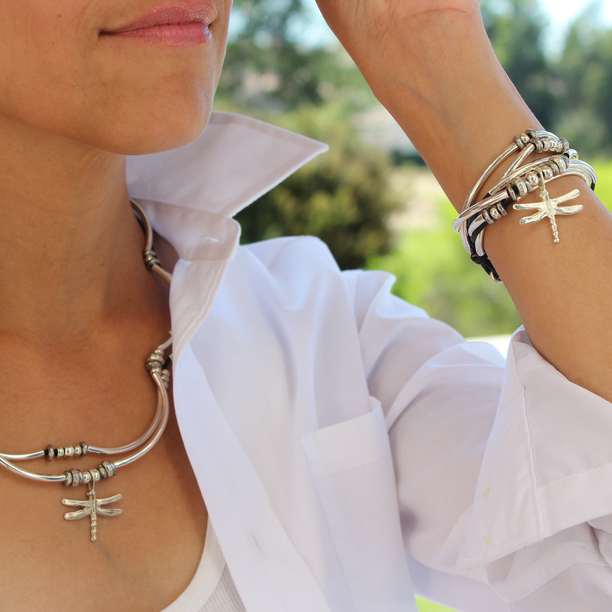 Person wearing a silver necklace and bracelets with a blurred outdoor background