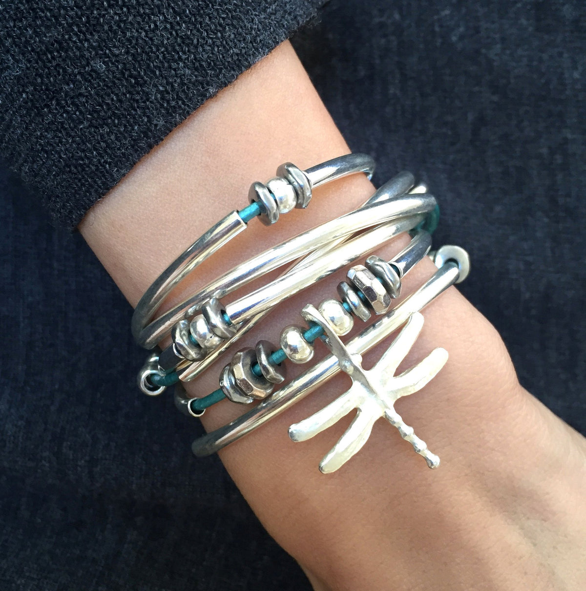 Close-up of a wrist wearing multiple silver bracelets on a dark background