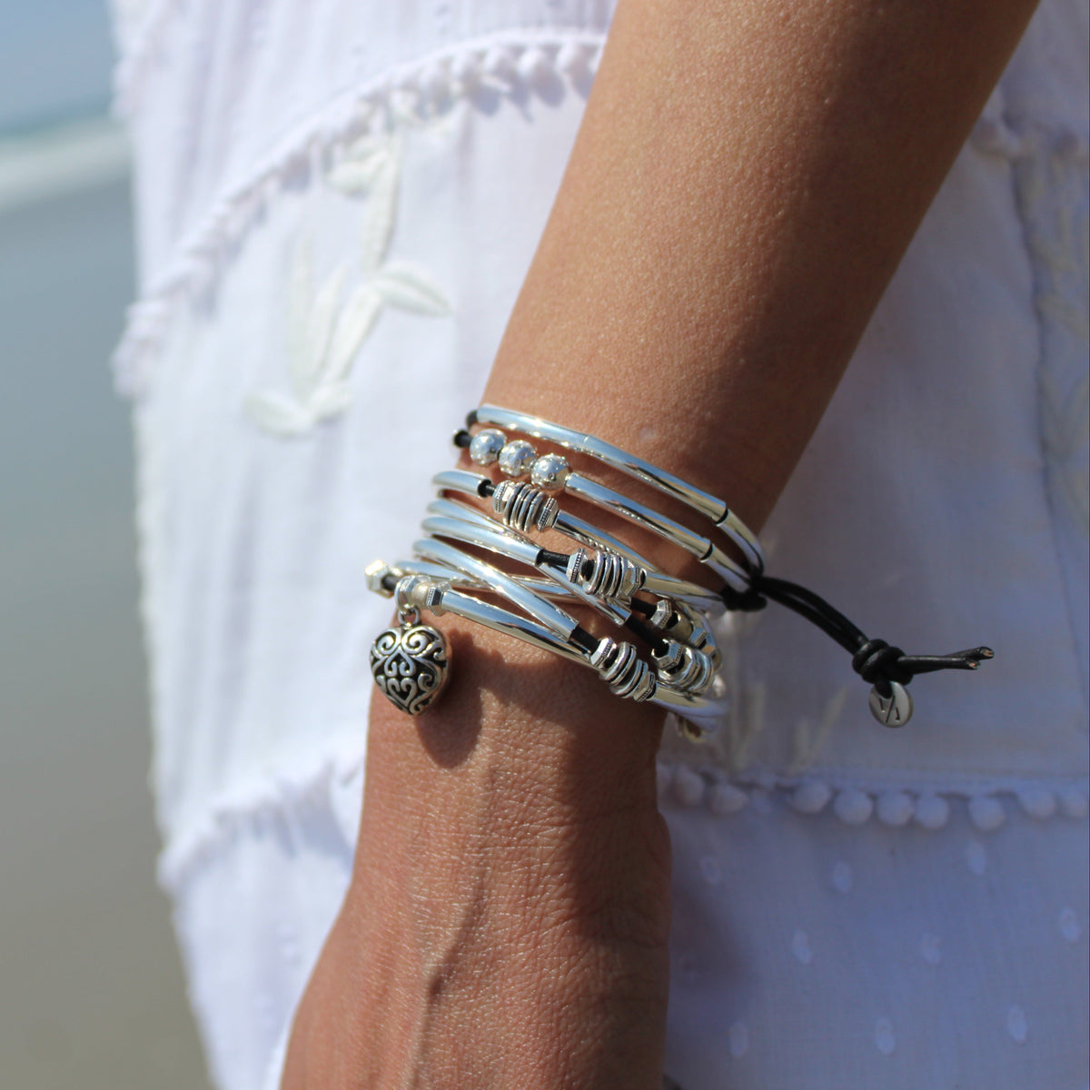 Close-up of a person's wrist wearing multiple silver bracelets with a blurred beach background