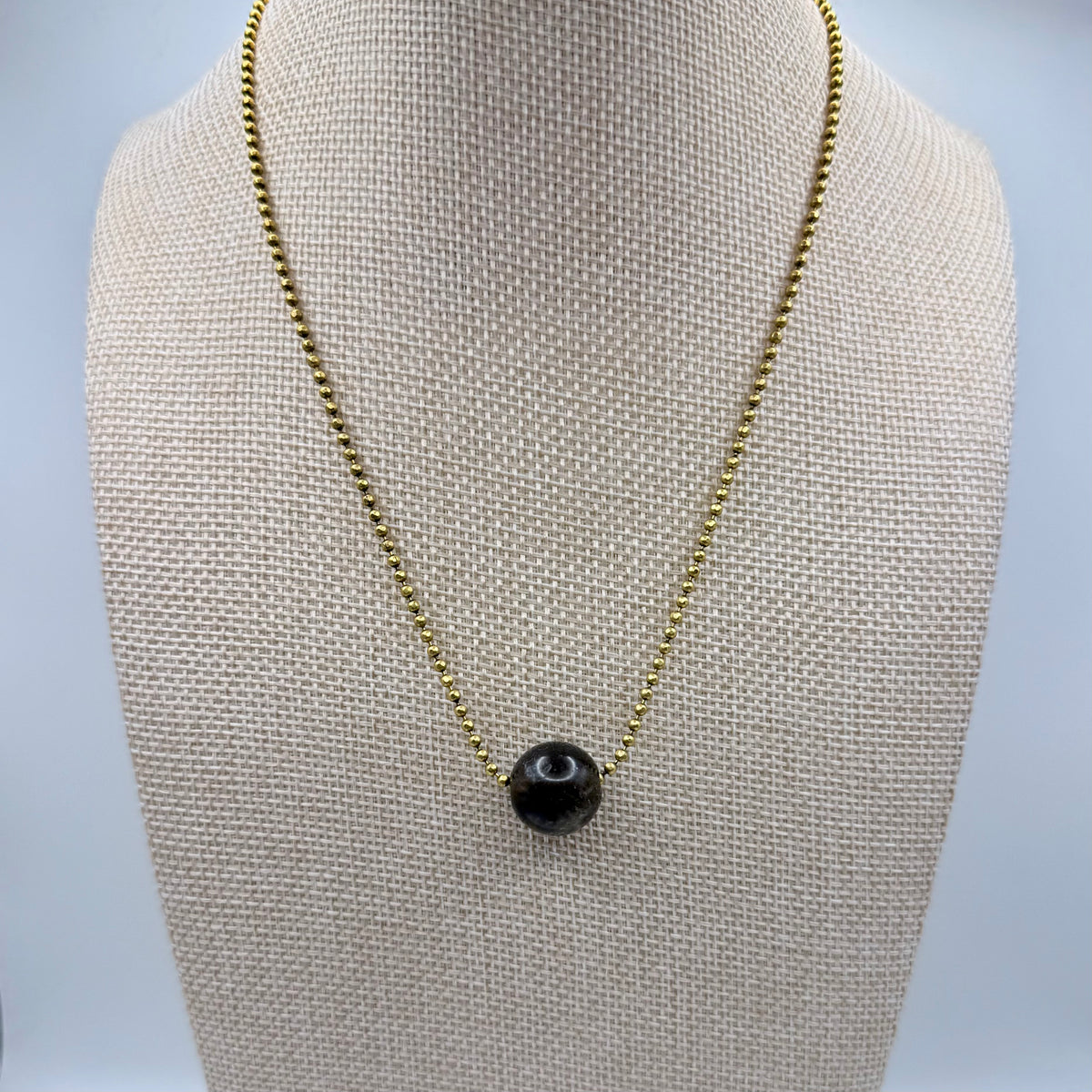Necklace with a black pendant on a mannequin bust against a light gray background