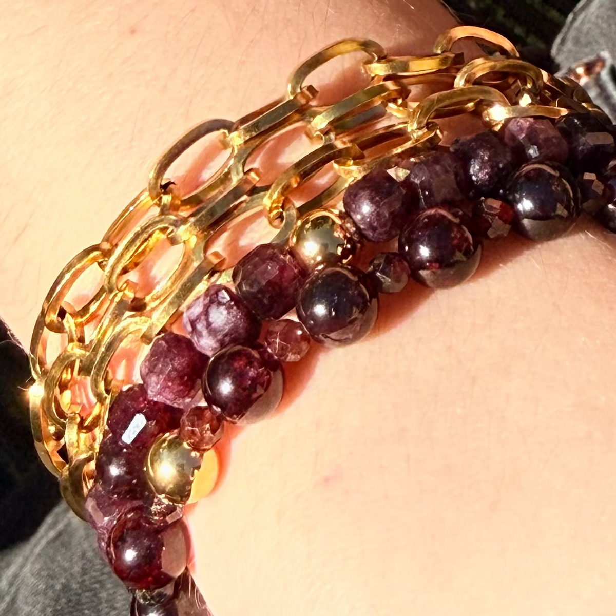 Gold chain and purple beaded bracelet on a wrist