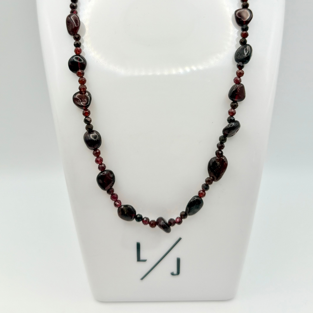 Necklace with red and black beads on a white stand with 'LJ' logo.