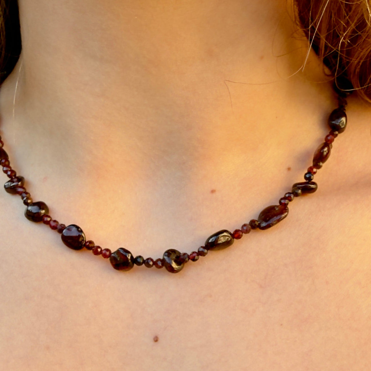Close-up of a person wearing a dark beaded necklace with a blurred background
