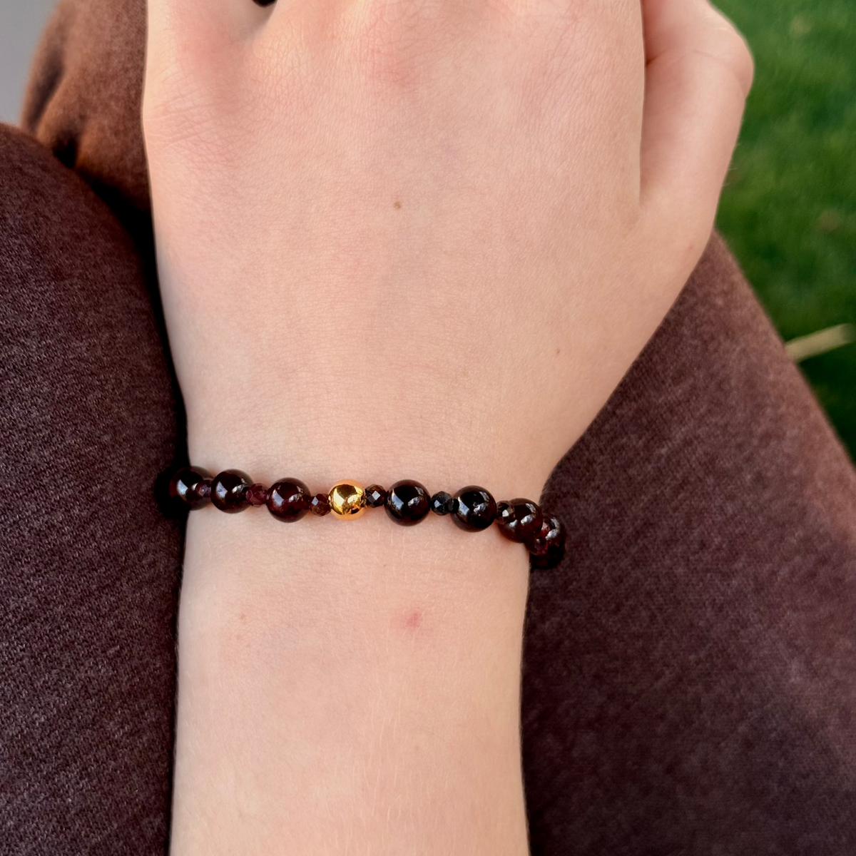 Hand wearing a beaded bracelet with a blurred natural background