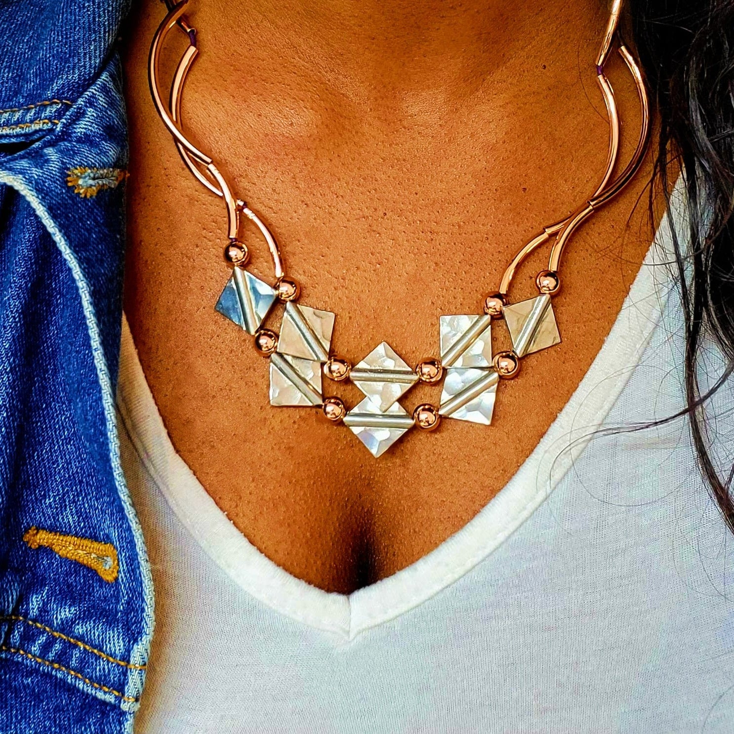 Necklace with geometric pendants worn by a person, with a blue denim jacket and white shirt in the background.