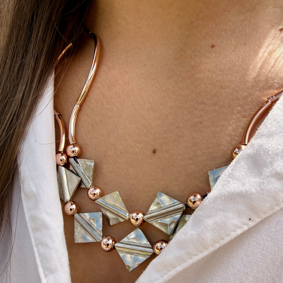 Close-up of a person wearing a gold and silver geometric necklace.