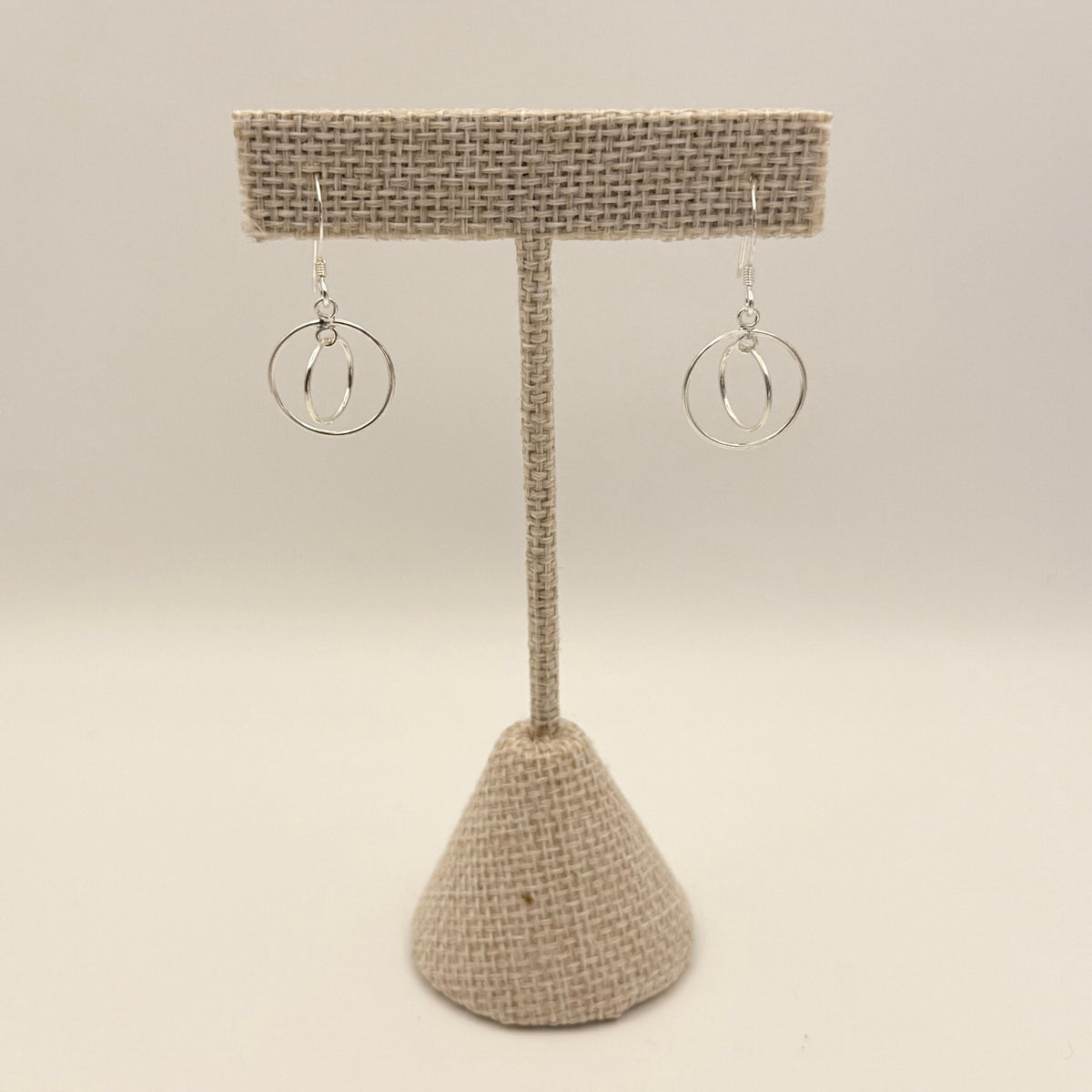 Pair of silver hoop earrings on a textured beige stand against a light background