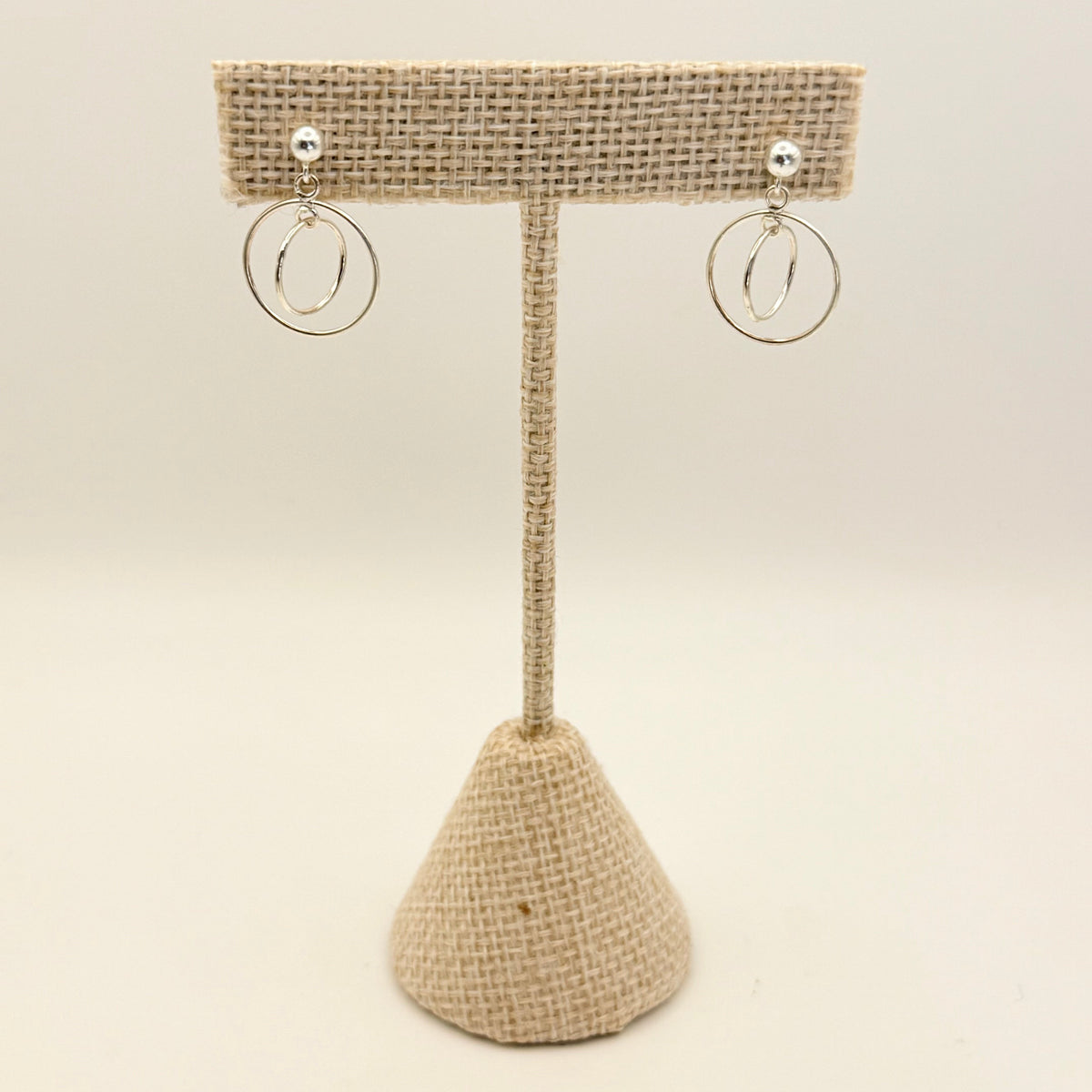 Beige woven earring stand with two silver hoop earrings on a beige background