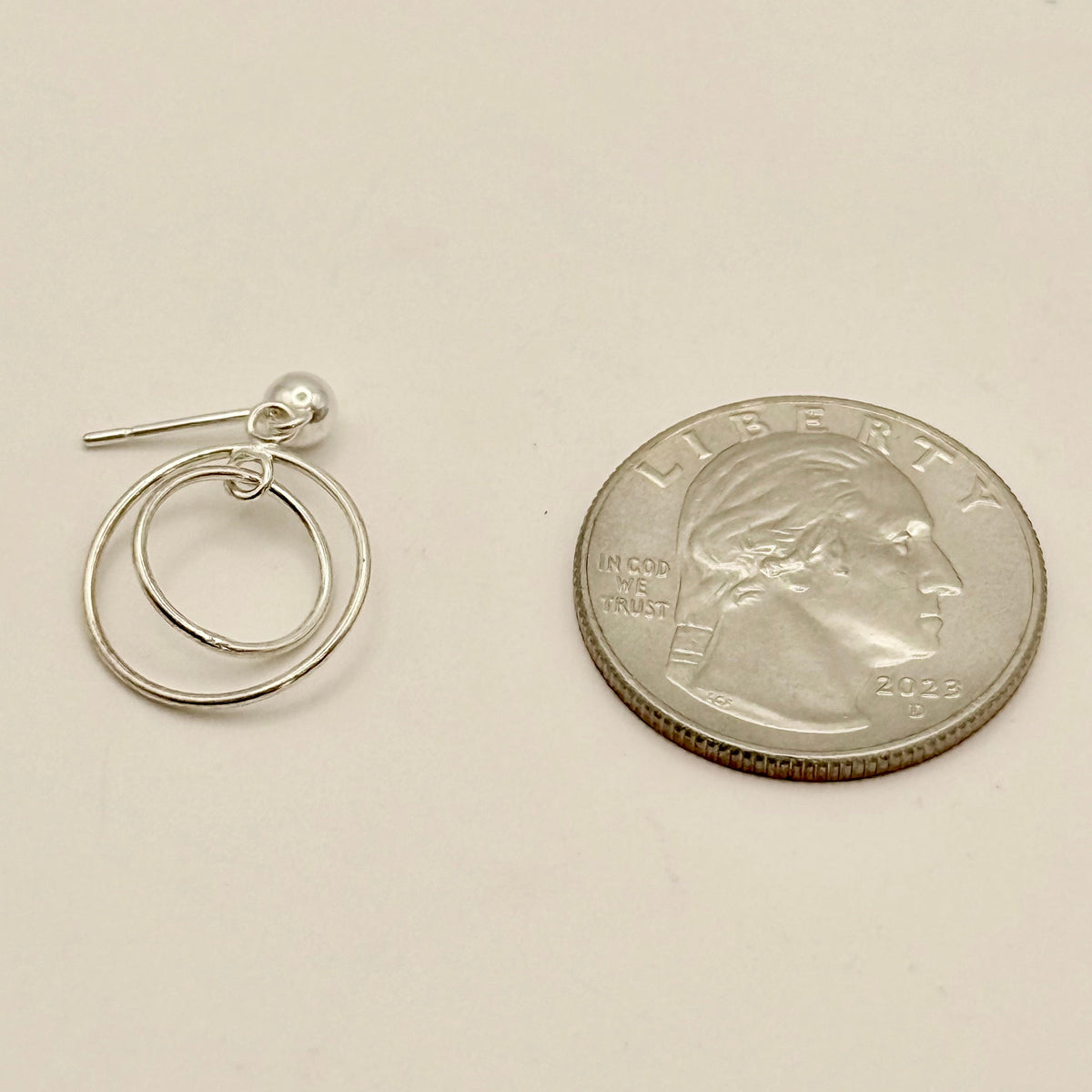 Silver hoop earrings next to a quarter on a beige background