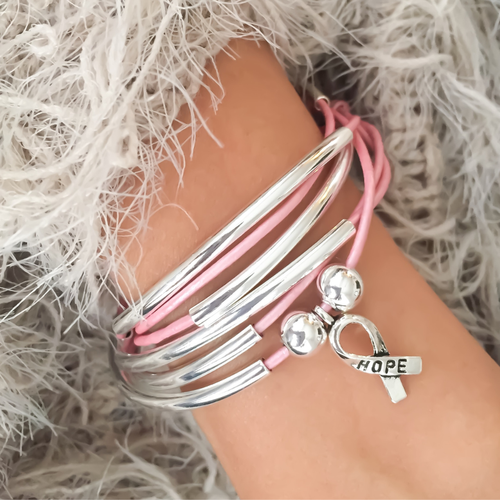 Silver and pink bracelets on a wrist with a 'HOPE' charm against a fluffy white background