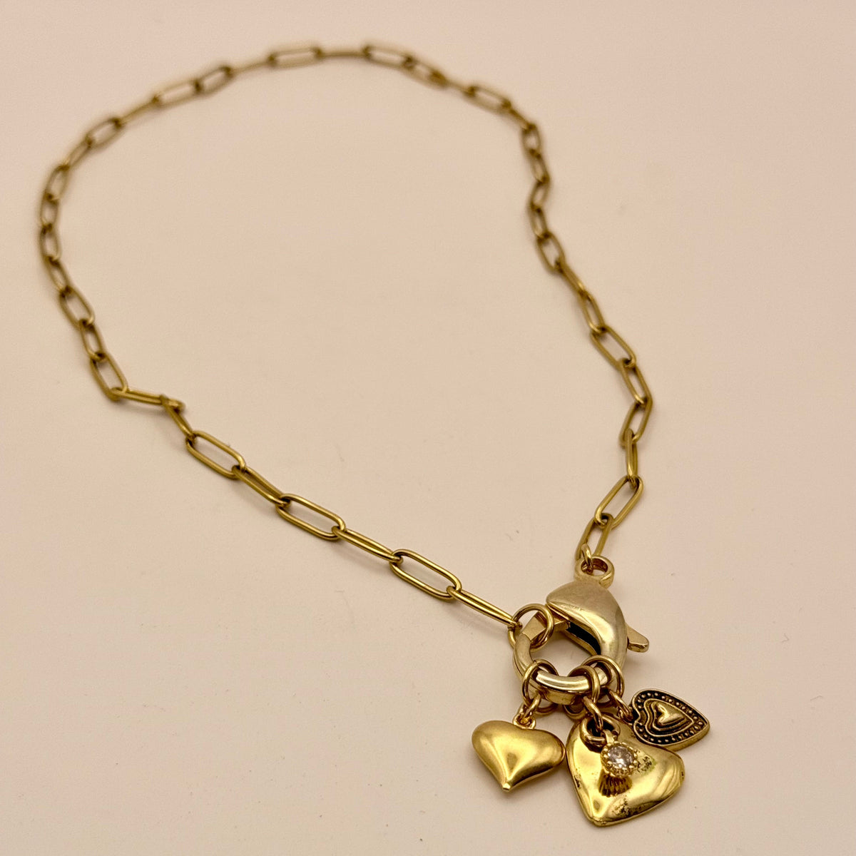 Gold bracelet with heart-shaped charms on a beige background