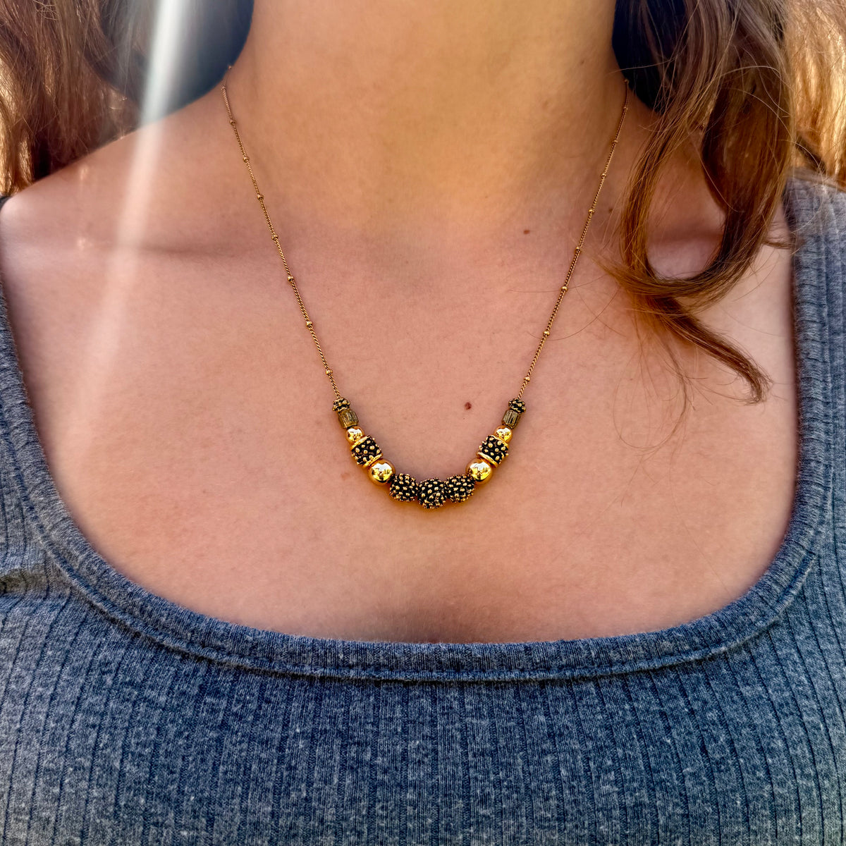 Necklace with gold and black beads worn by a person in a blue top.