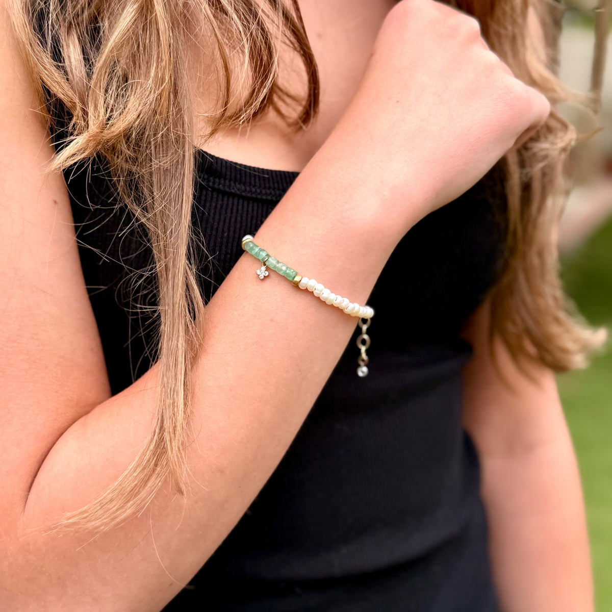 Close-up of a person wearing a bracelet with pearls and green beads.