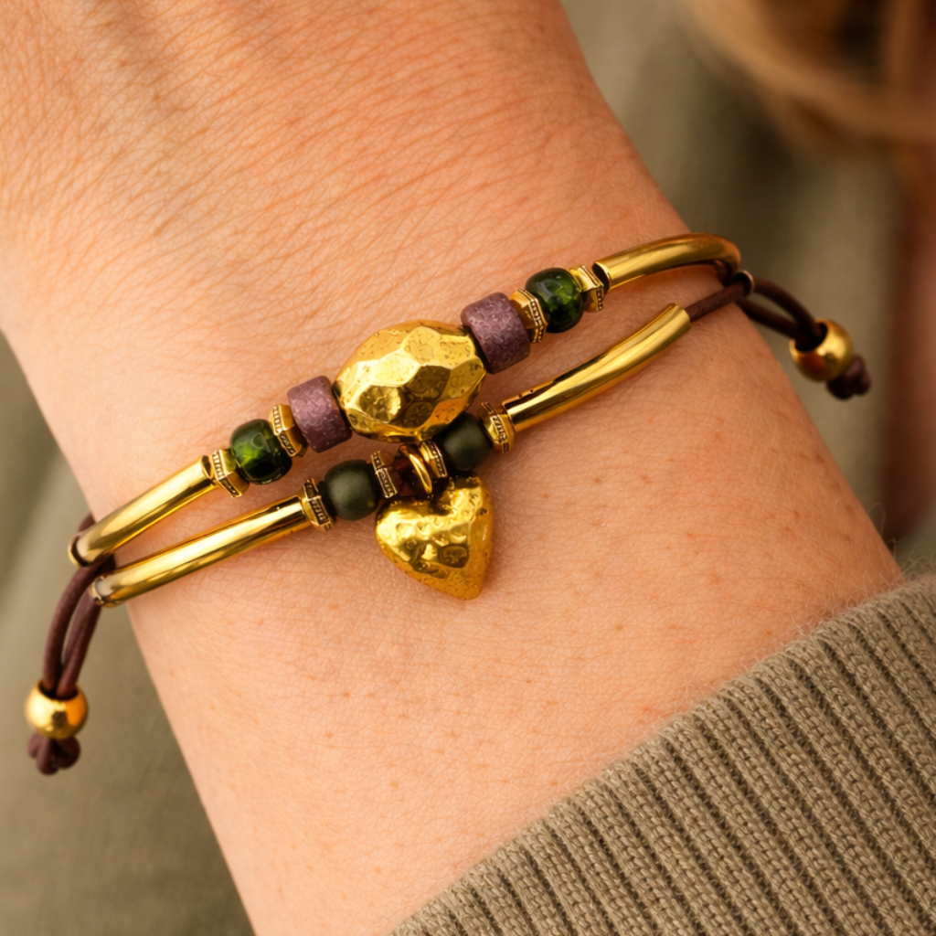 Close-up of a wrist wearing a gold bracelet with heart-shaped charm and green beads.