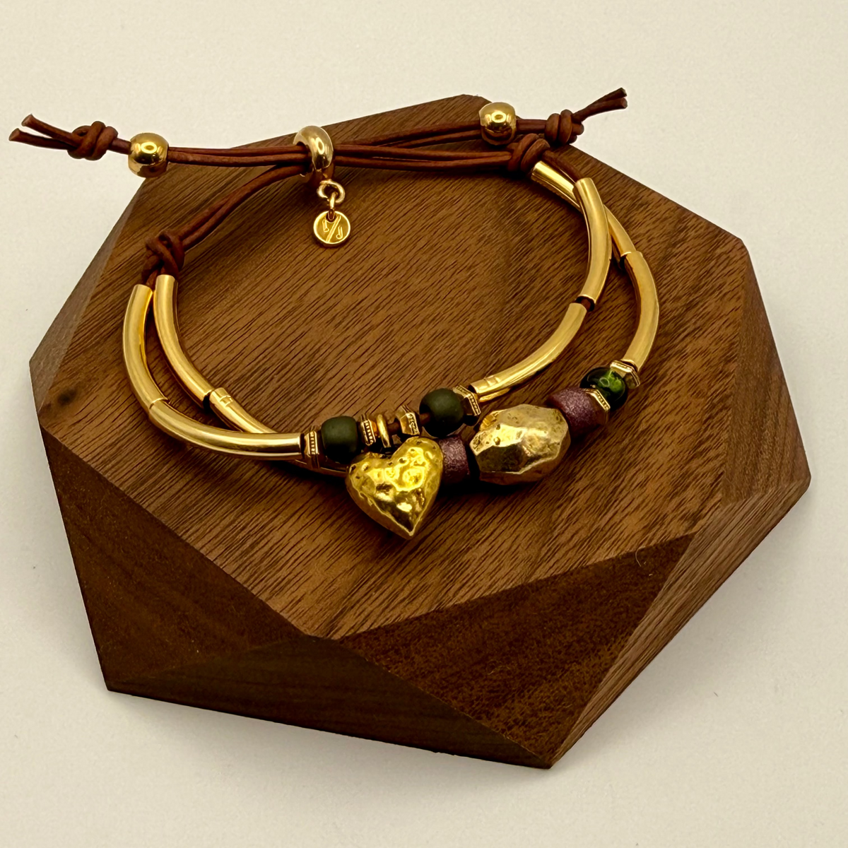 Gold bracelet with heart and bead details on a wooden stand