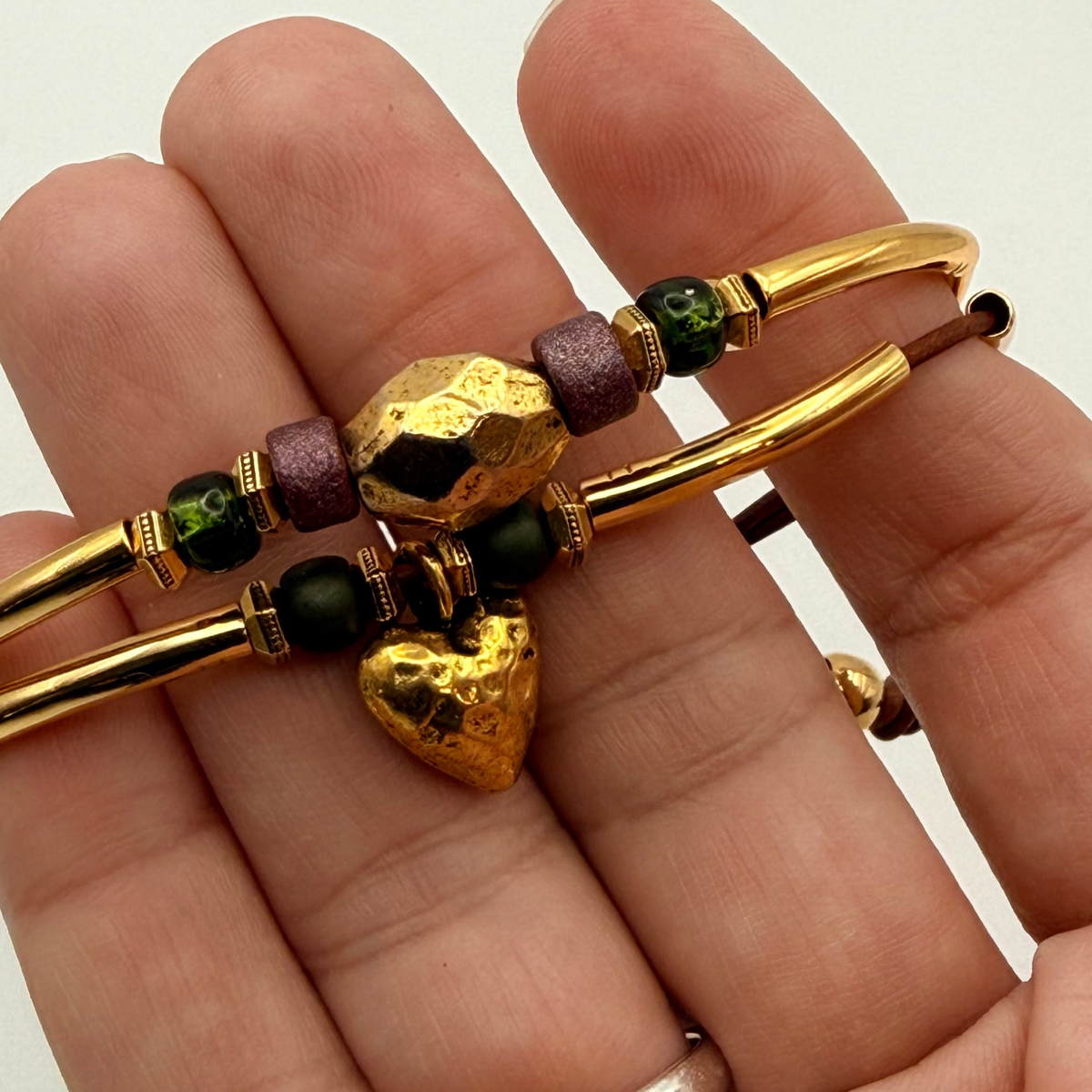 Gold bracelet with heart charm held in a hand against a white background
