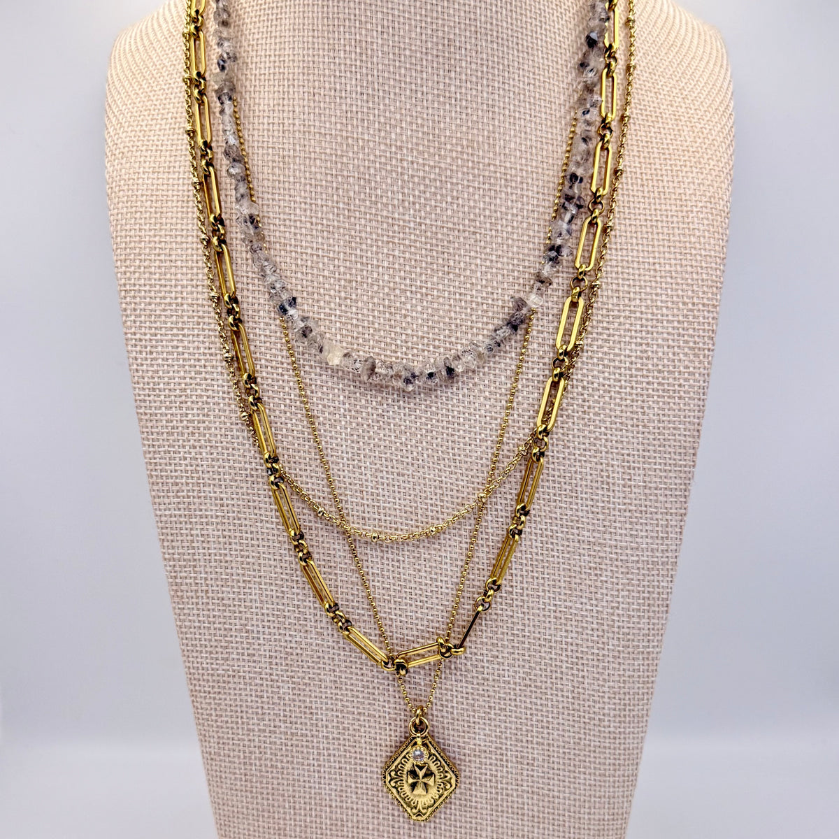 Gold necklaces with beads and a pendant on a mannequin bust against a gray background