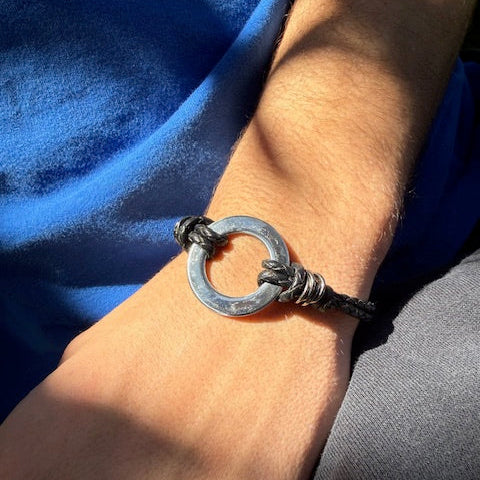 Bracelet with a circular metal clasp on a wrist against a blue fabric background