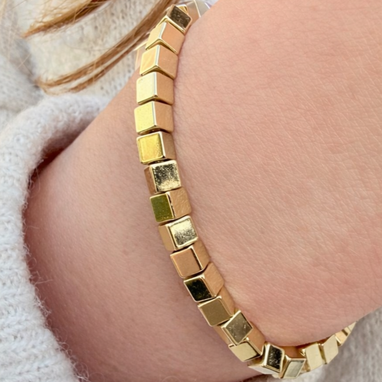 Gold bracelet on a wrist with a neutral background