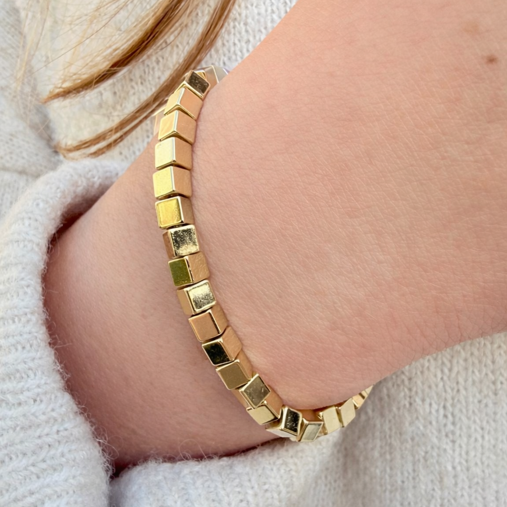Gold bracelet on a wrist with a neutral background