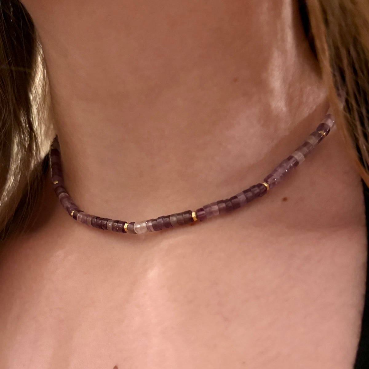 Close-up of a person wearing a beaded necklace with a neutral background