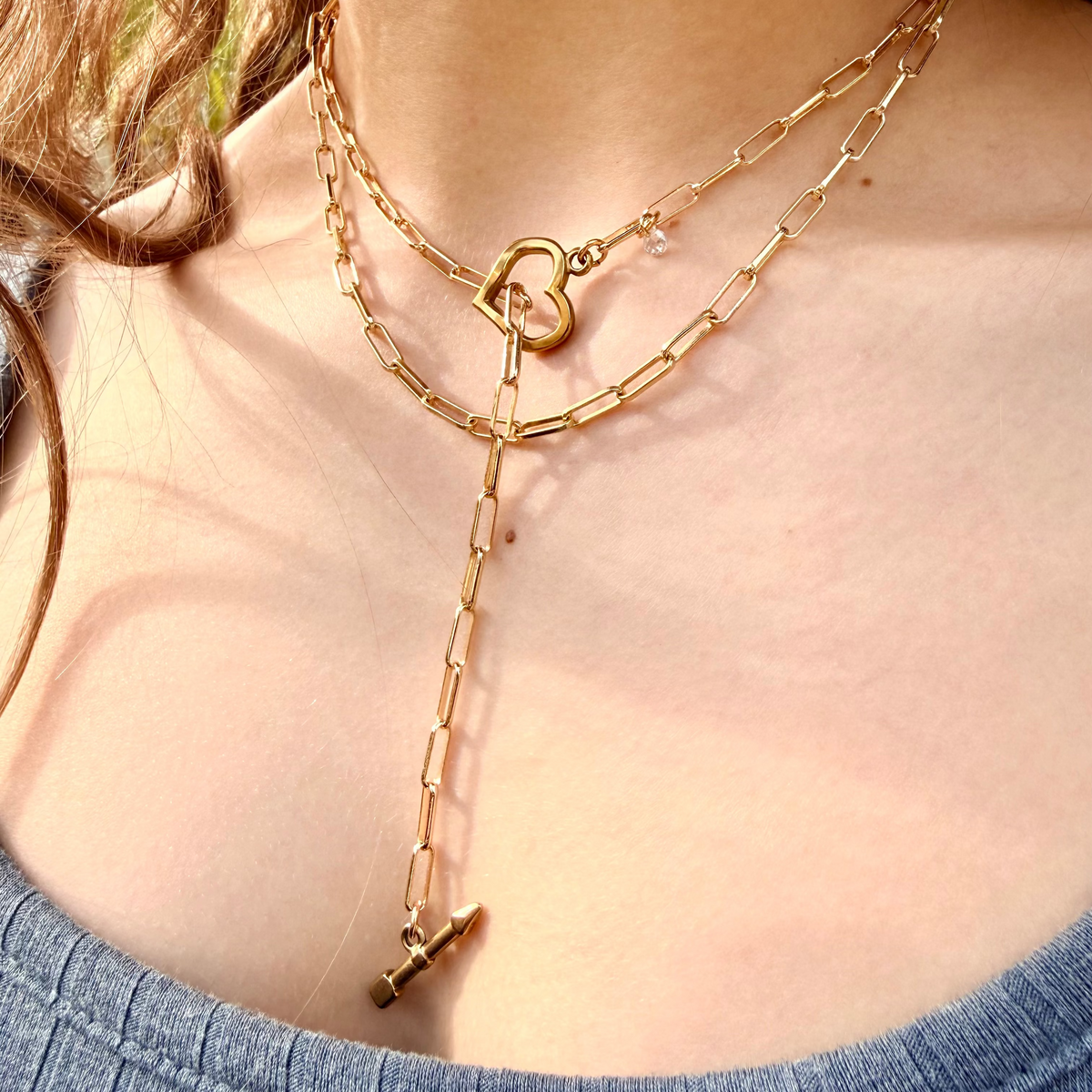 Gold chain necklace with a heart clasp worn by a person