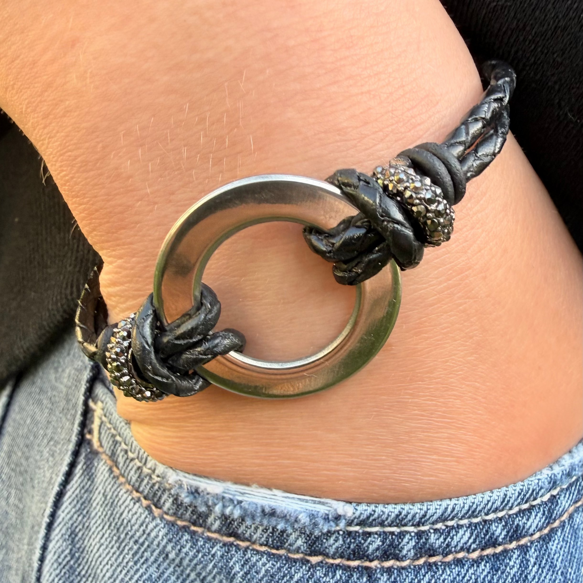 Bracelet with metal ring and braided design on wrist, wearing denim jeans.