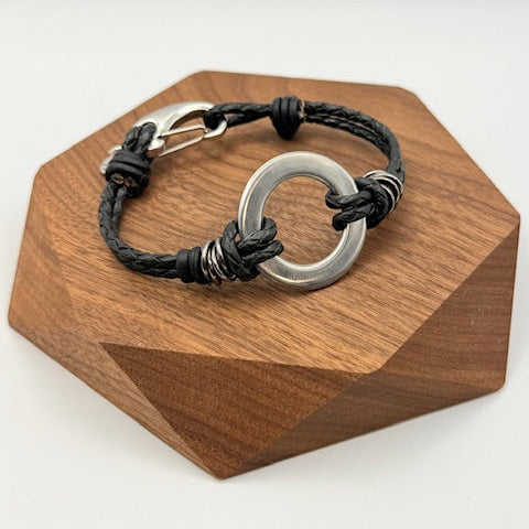 Bracelet with black cord and silver circular clasp on a wooden stand