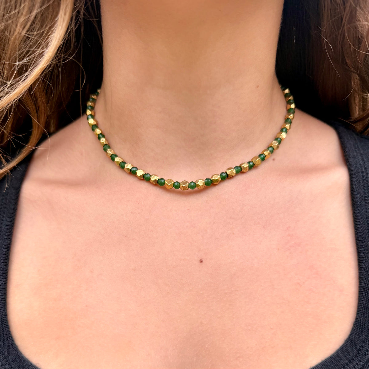 Close-up of a person wearing a green and gold beaded necklace.