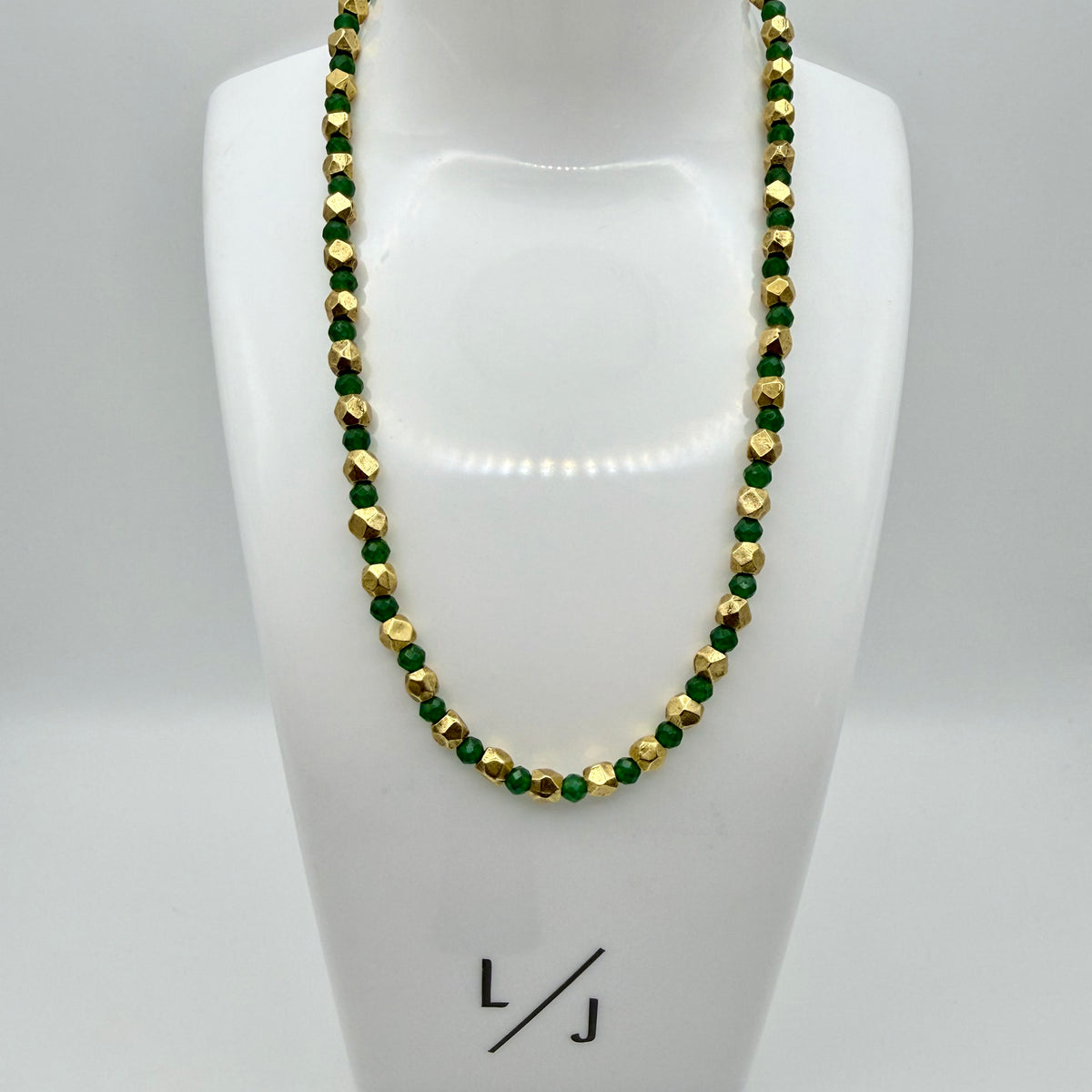 Necklace with green and gold beads on a mannequin bust with 'LJ' branding.