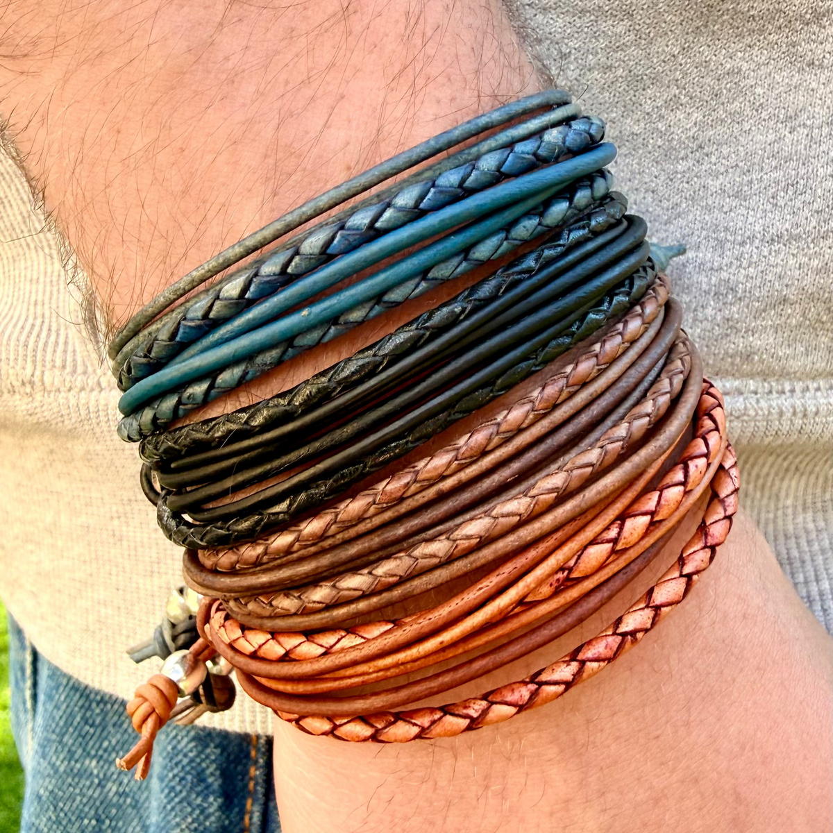 Multiple braided leather bracelets on a wrist with a blurred background