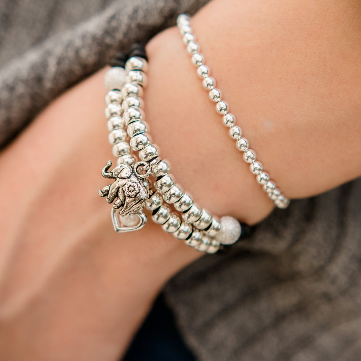 Close-up of a wrist wearing two silver beaded bracelets with charms.