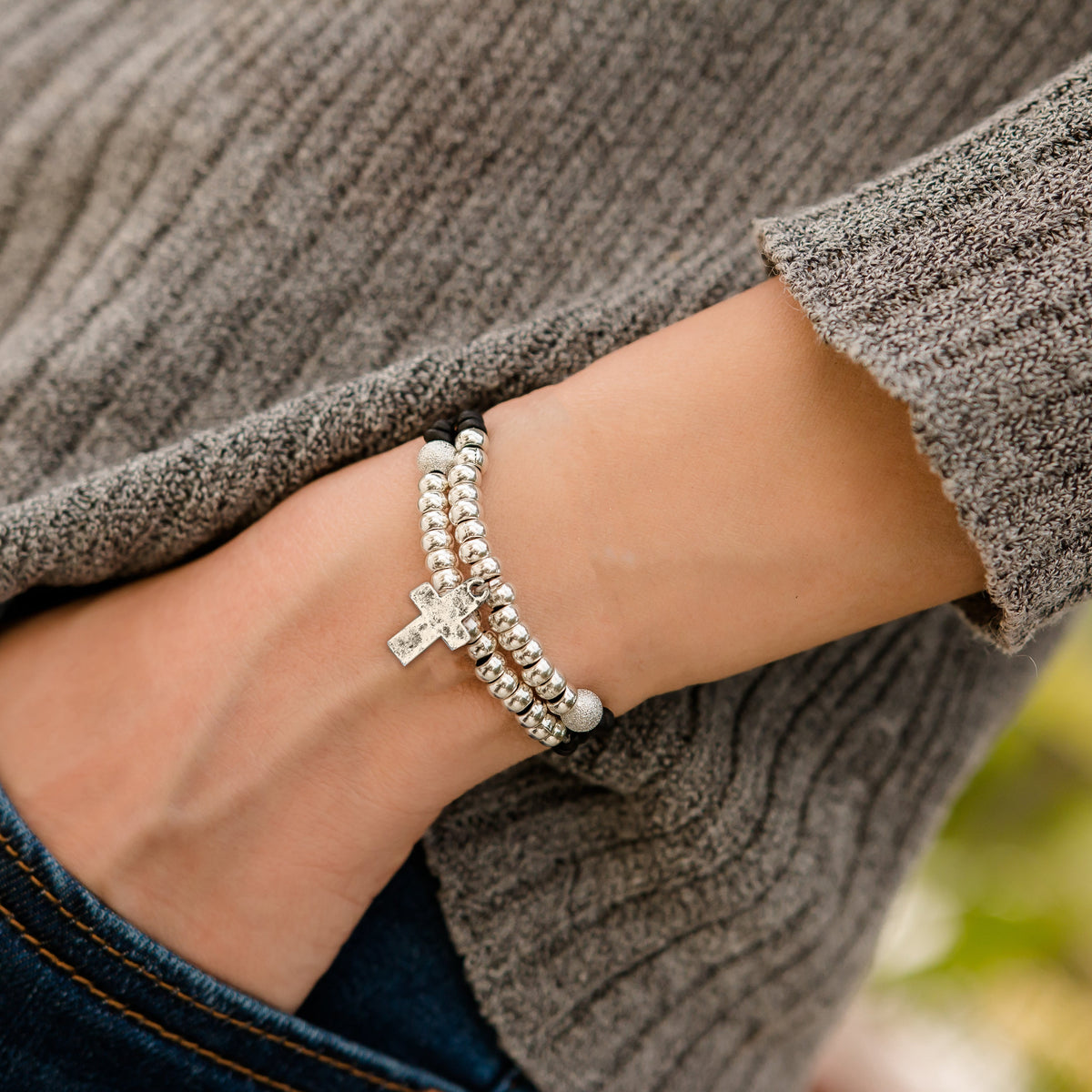 Close-up of a person wearing two silver bracelets on a blurred background