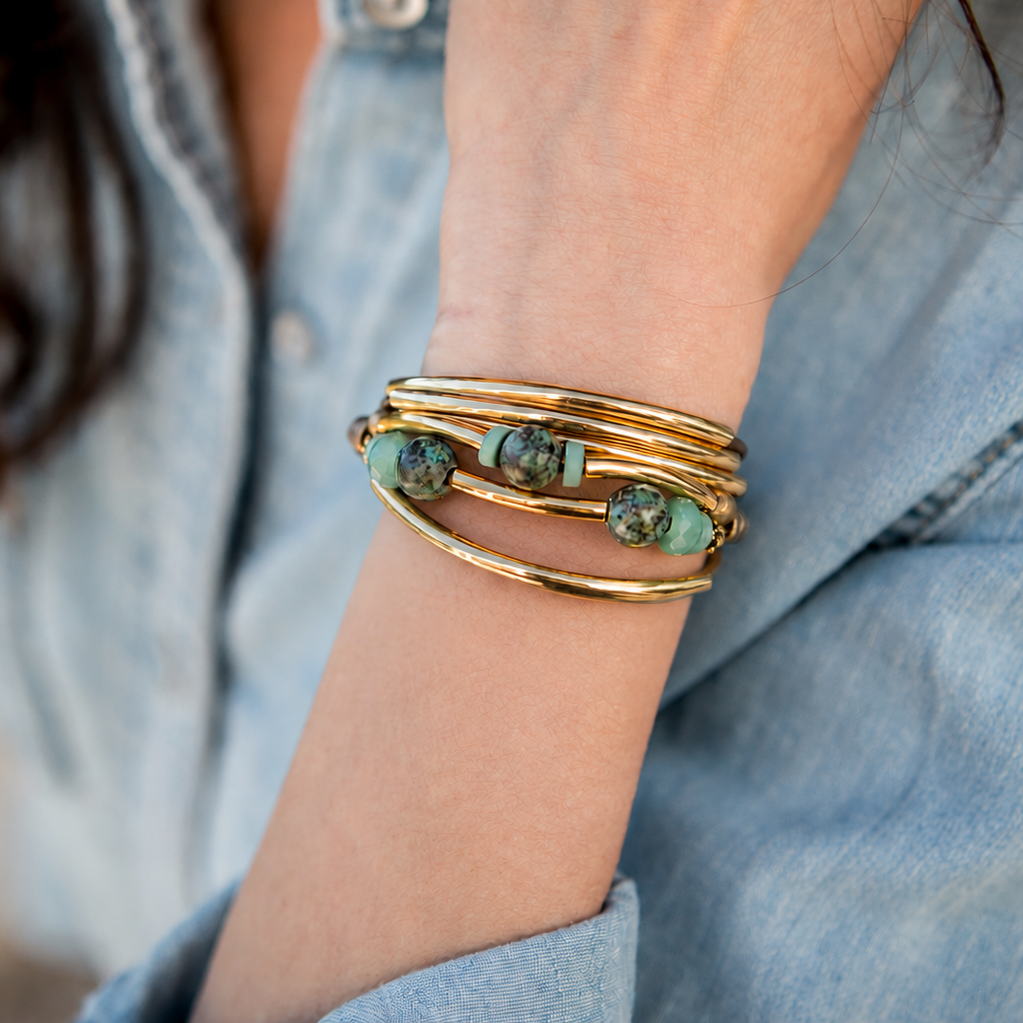 Close-up of a person wearing a gold bracelet with turquoise stones on a blurred background