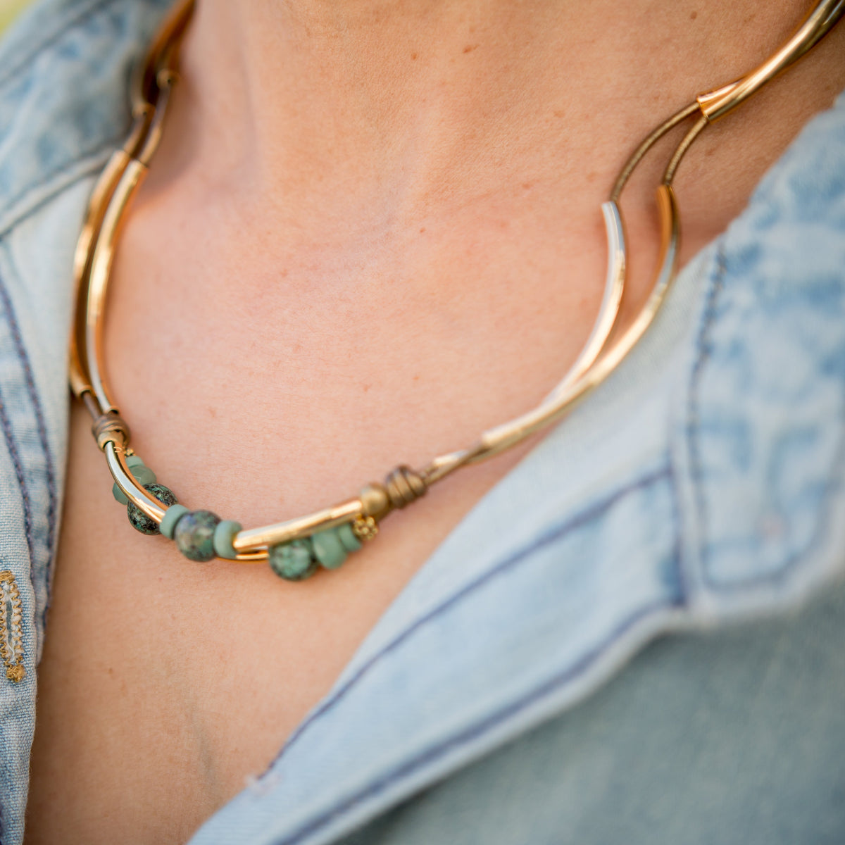 Close-up of a person wearing a gold and green beaded necklace with a denim jacket.