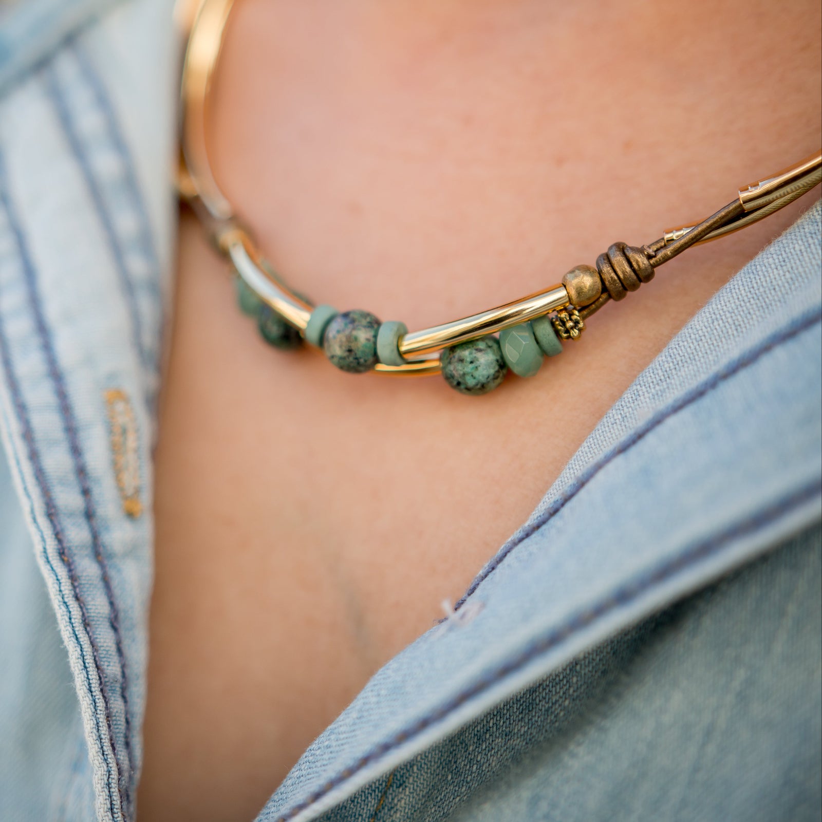 Gold necklace with green beads worn by a person in a denim jacket.