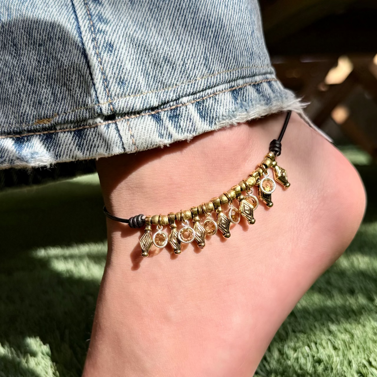 Gold anklet on a foot with denim jeans and grass in the background