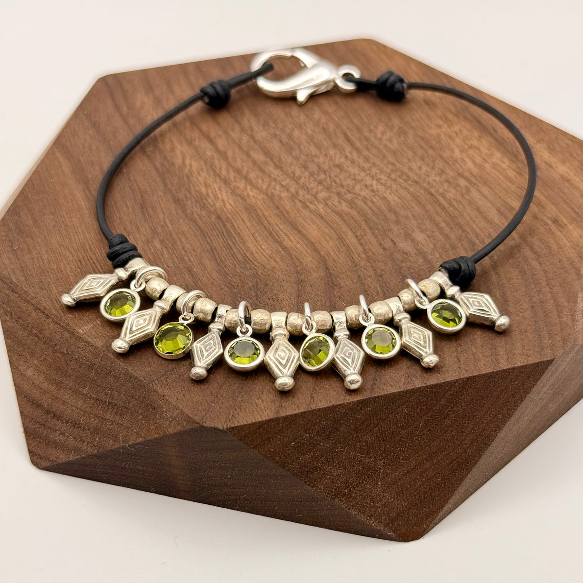 Bracelet with green gemstones and silver accents on a wooden stand