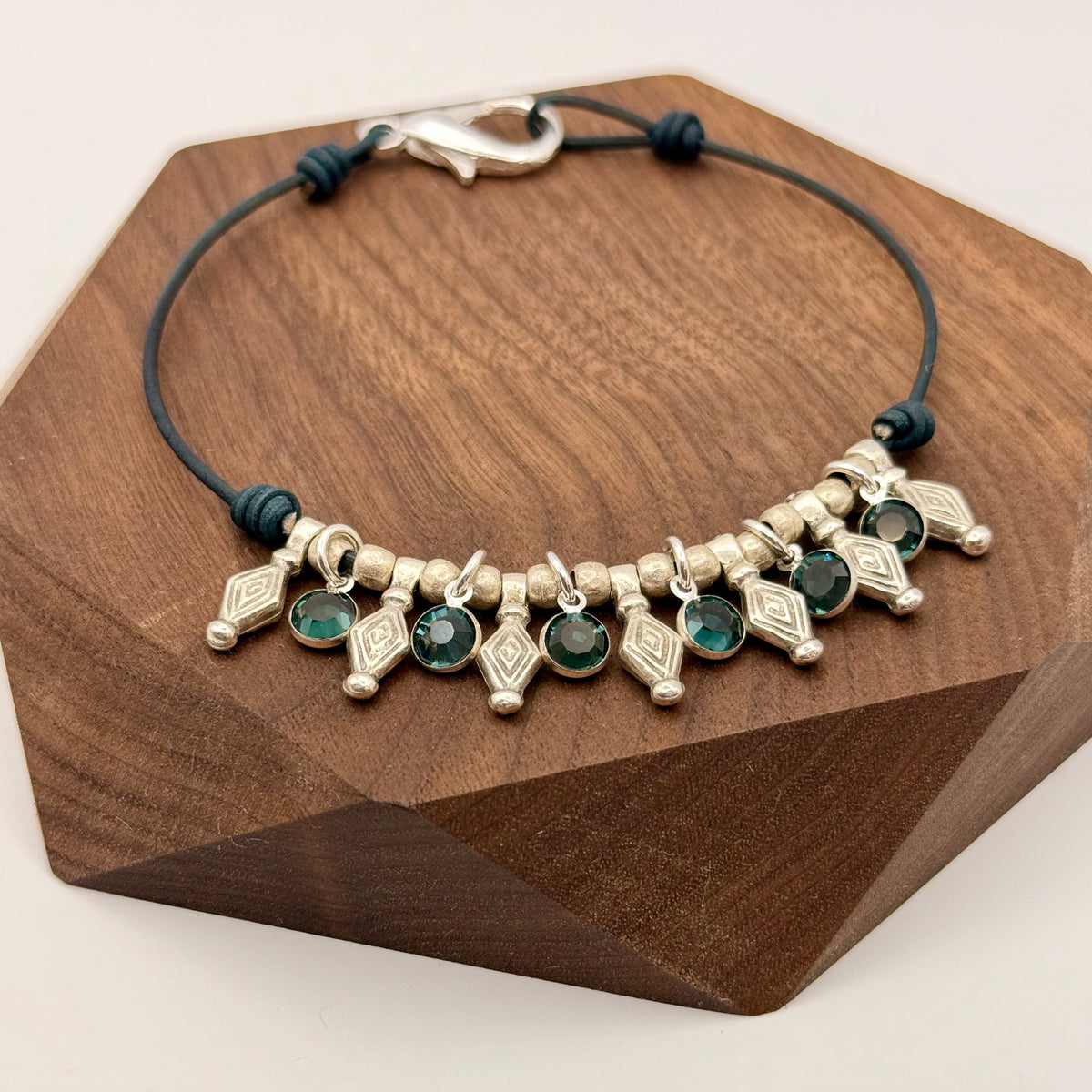 Bracelet with green gemstones and silver accents on a wooden stand