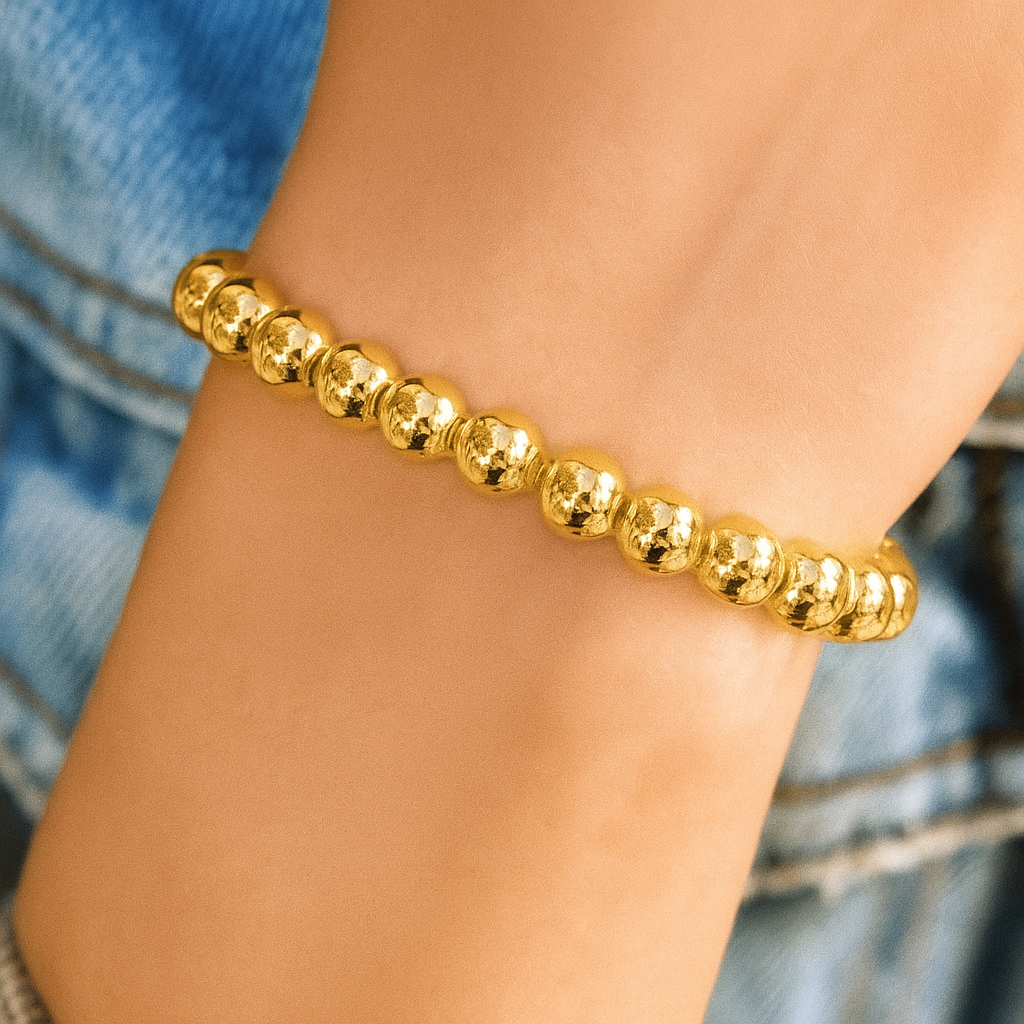Gold beaded bracelet on a wrist with a blurred denim background