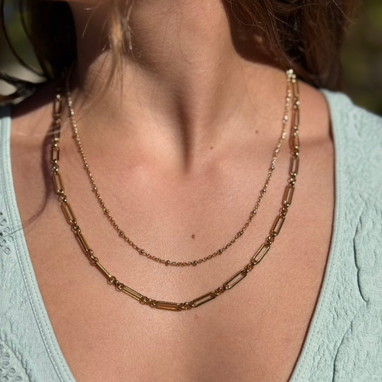 Close-up of a person wearing a gold chain necklace with a blurred background