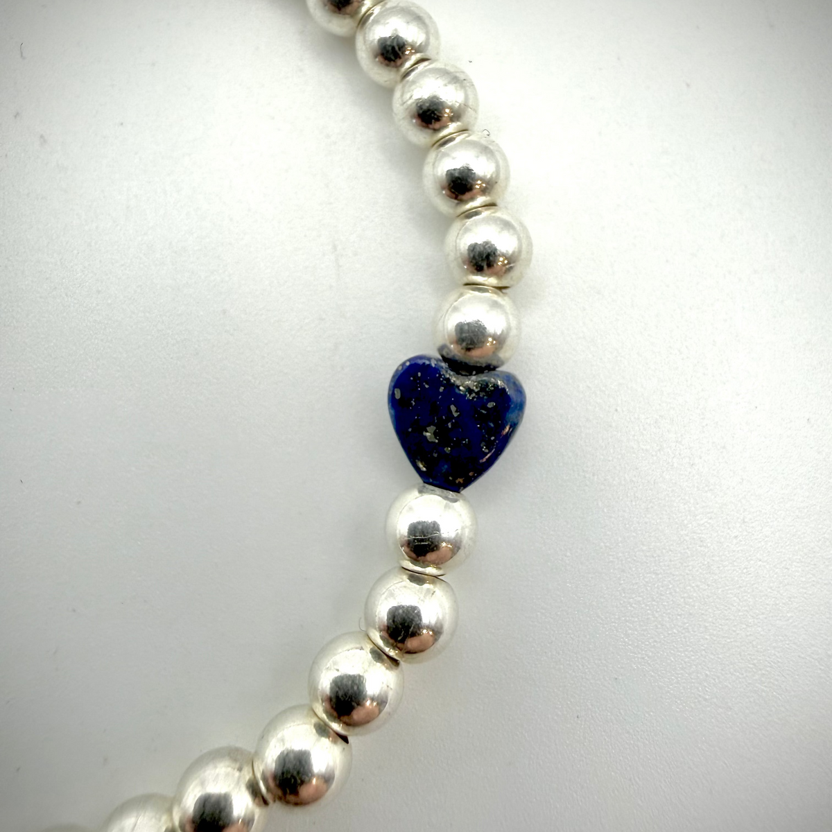 Silver beaded bracelet with a blue heart-shaped charm on a white background
