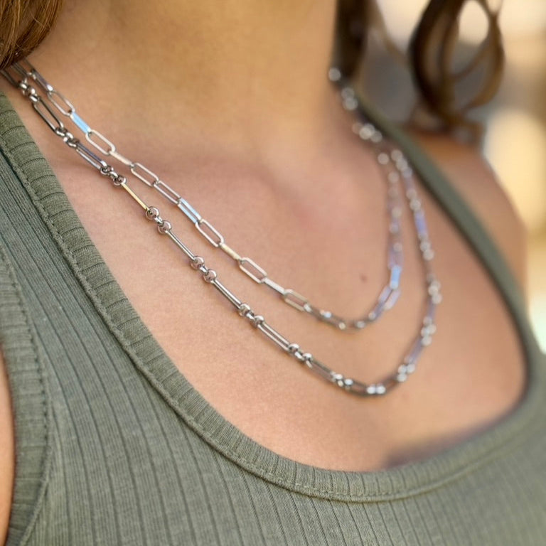 Close-up of a person wearing two silver necklaces with a blurred background