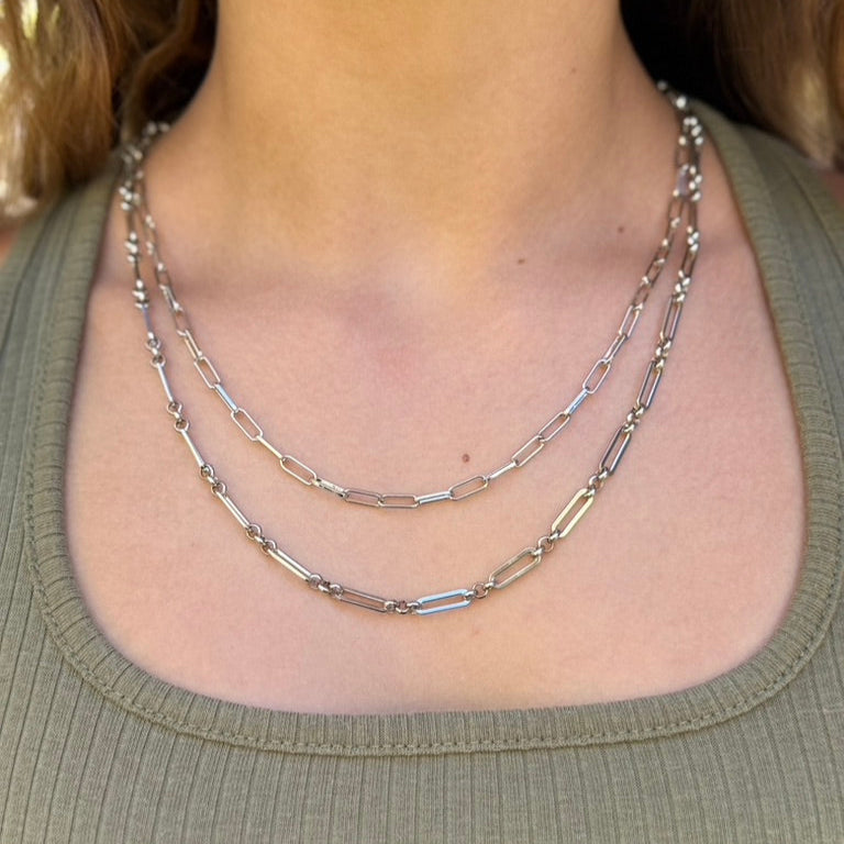 Person wearing a silver chain necklace on a plain background